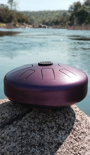 a purple steel tongue drum sitting in the sun by a lake